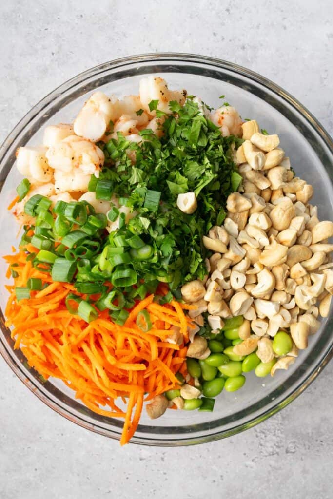 shrimp, cashews, shredded carrots, chopped green onion, chopped cilantro, and edamame in a glass bowl.