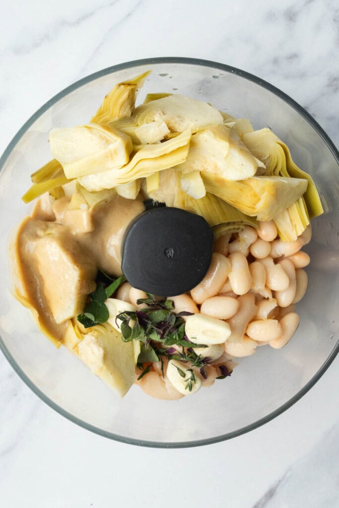 artichoke hearts, white beans, tahini, garlic and fresh herbs in a food processor bowl. 