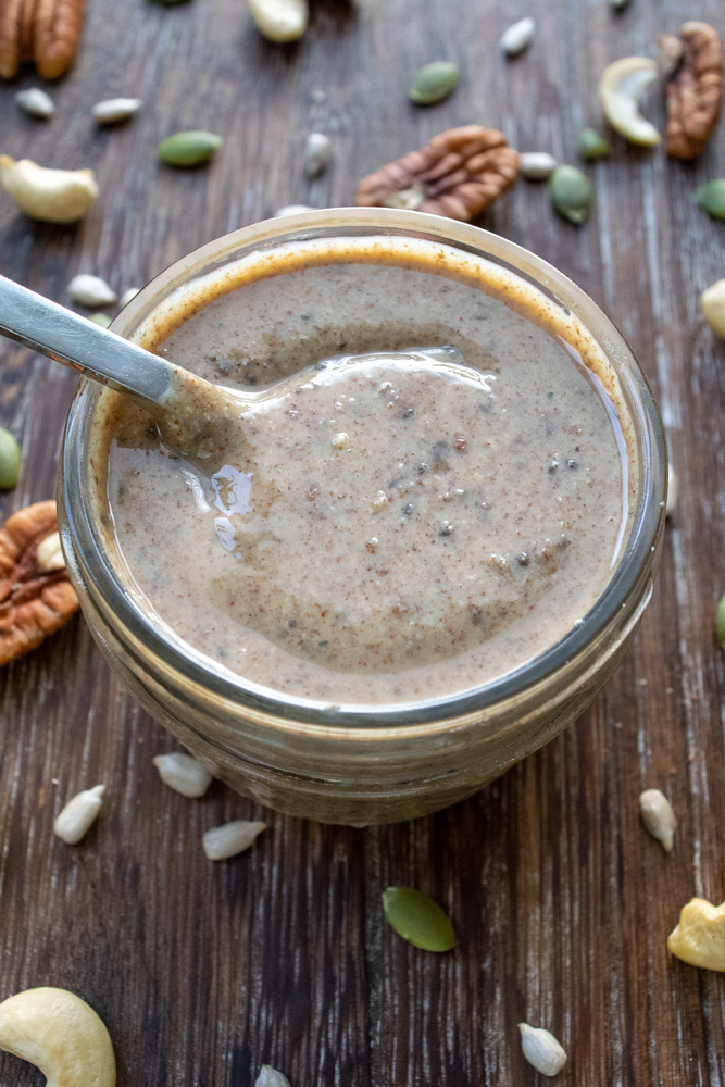 a jar of super seed pecan cashew butter surrounded by cashews, pecans and pumpkin seeds.