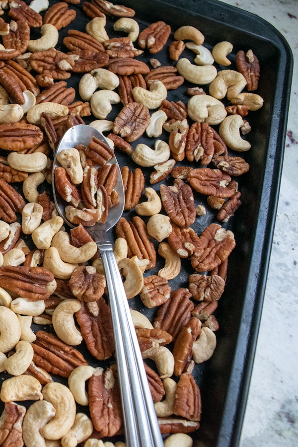 a baking sheet of roasted pecans and cashews with a silver spoon.