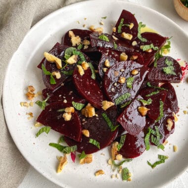 a white plate with marinated beets topped with walnuts and mint.