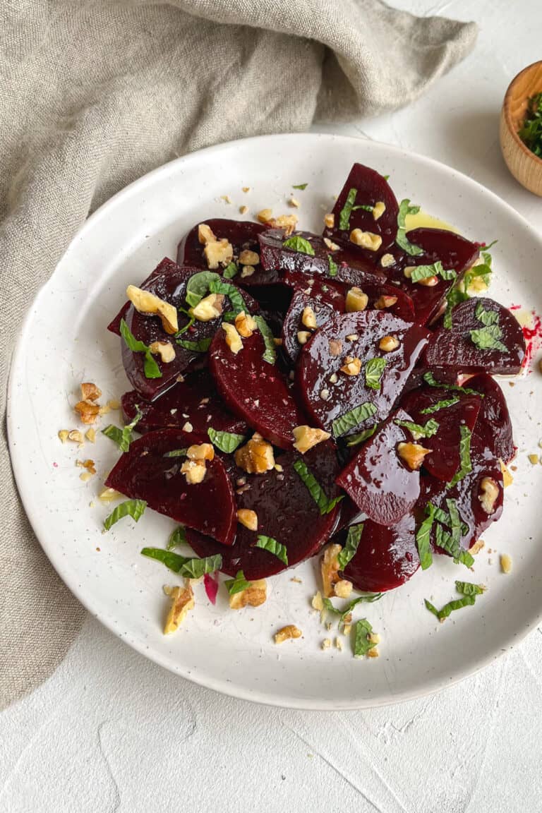 a white plate with marinated beets topped with walnuts and mint.