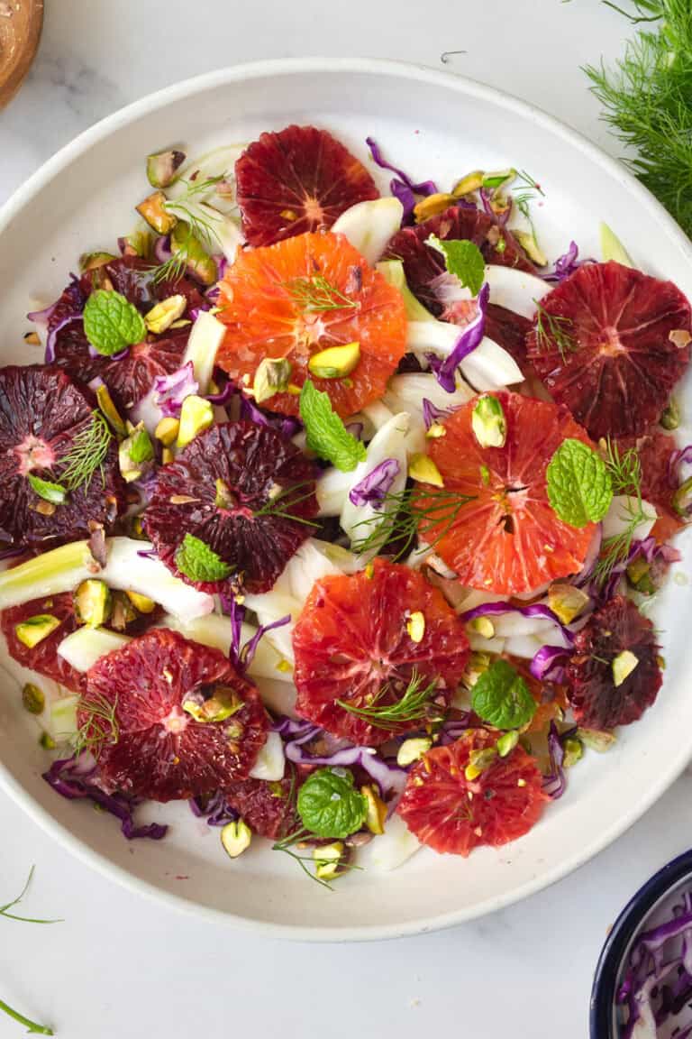 a white plate with a layered blood orange and fennel salad garnished with pistachios, mint and fennel fronds.