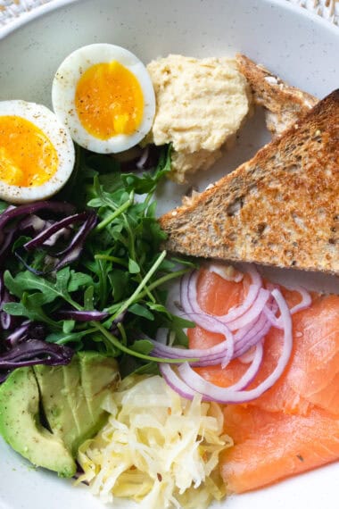 breakfast plate with boiled eggs, greens, avocado, sauerkraut, smoked salmon and toast