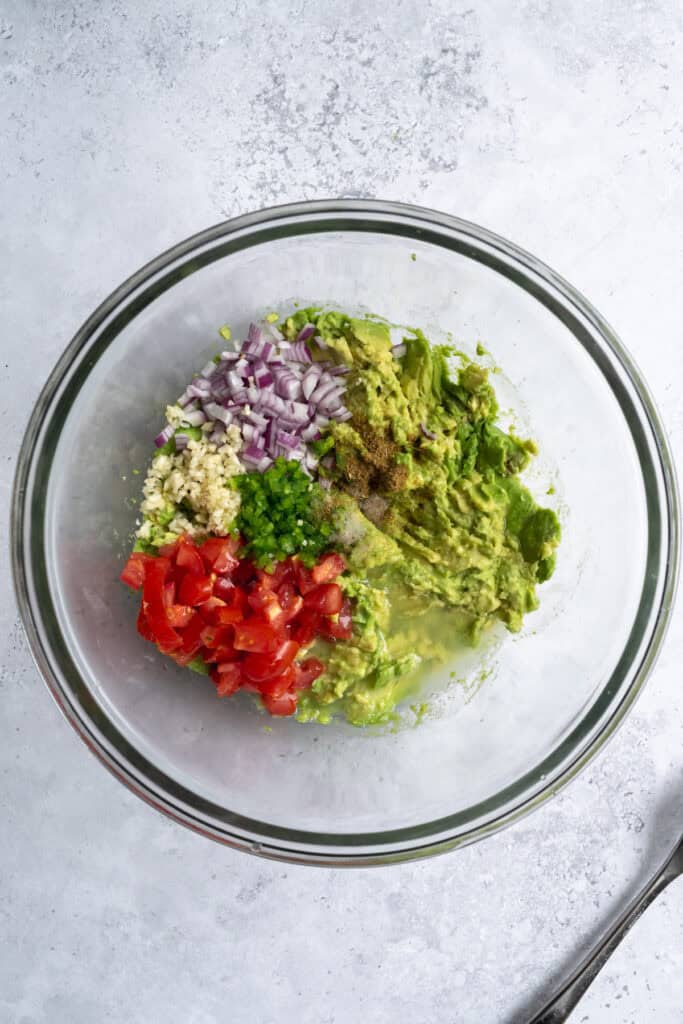 a bowl of mashed avocado with remaining avocado ingredients.