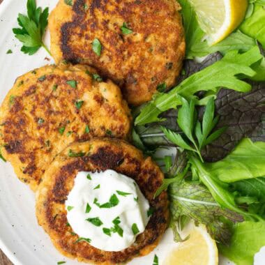 three salmon patties topped with chopped parsley and yogurt, and a green salad on a white plate.